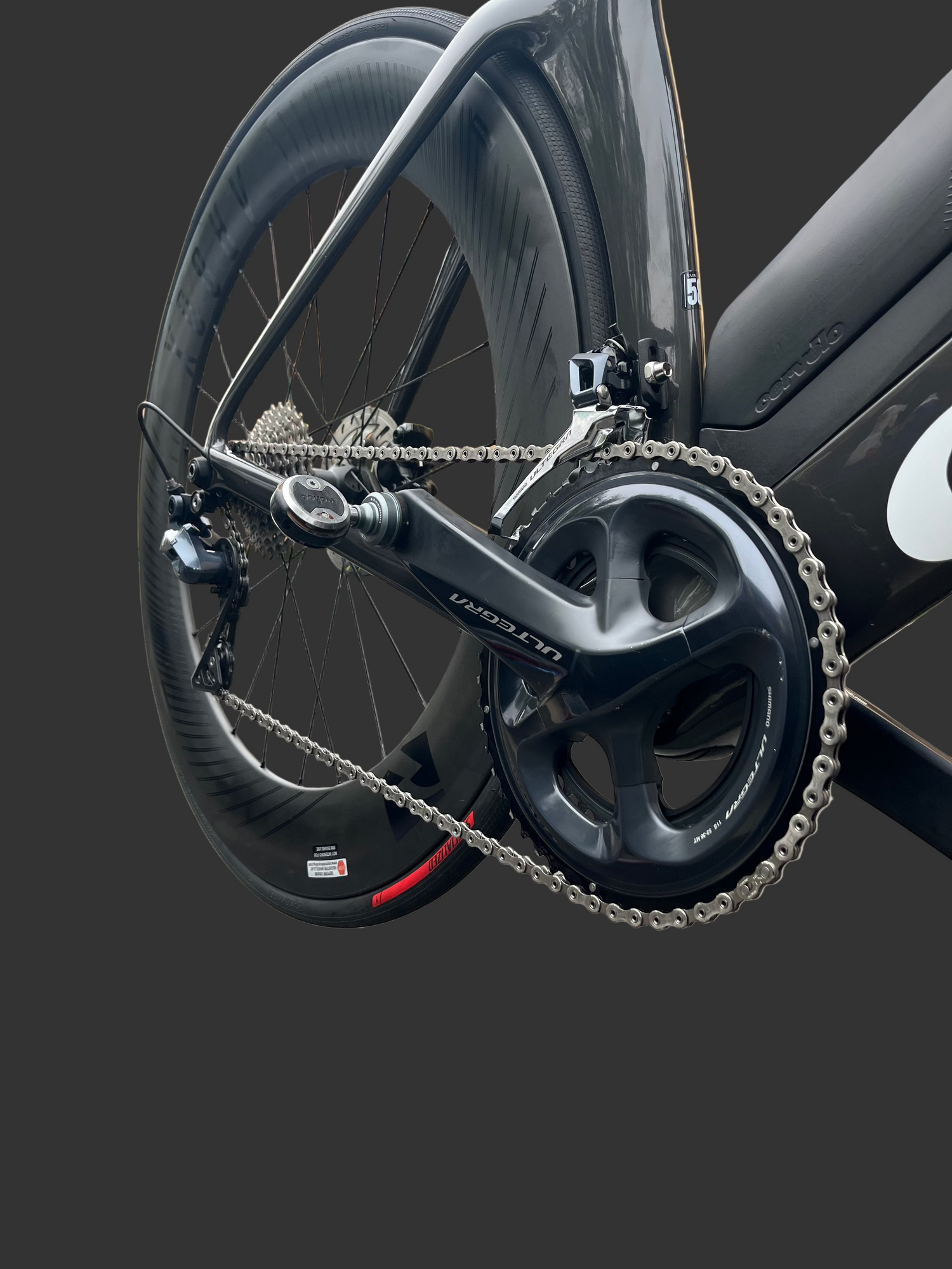 Close-up of a bicycle chain and gear system on a road with buildings in the background